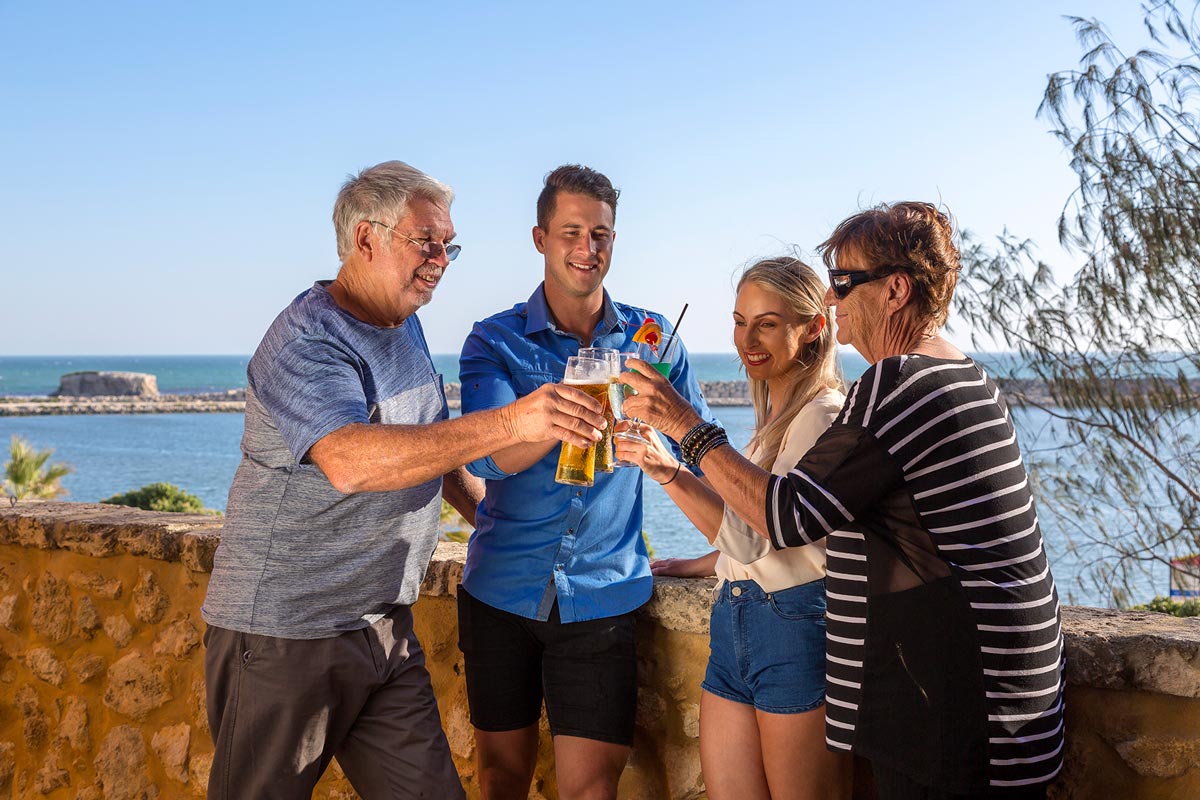 Three people toasting with beer on a balcony overlooking Atlantis Beach.