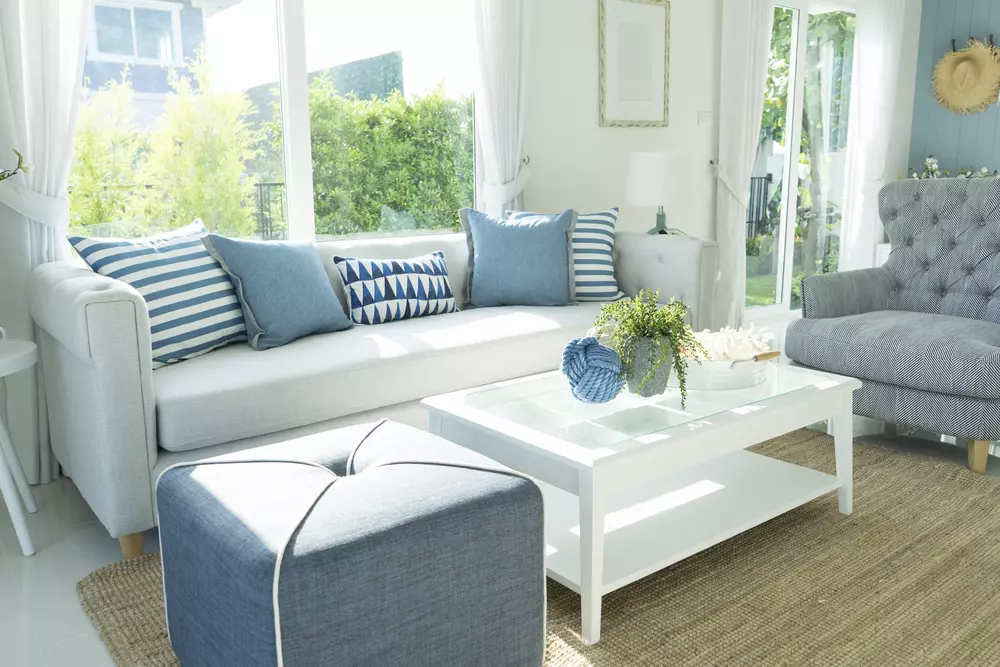 A cozy living room in a house and land package with a couch, chair, coffee table, rug, window, and door.