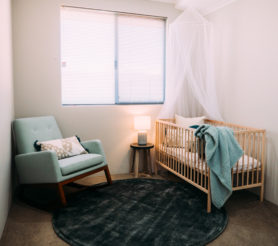 A cozy baby's room with a crib, rocking chair, and a window overlooking the serene Atlantis Beach.